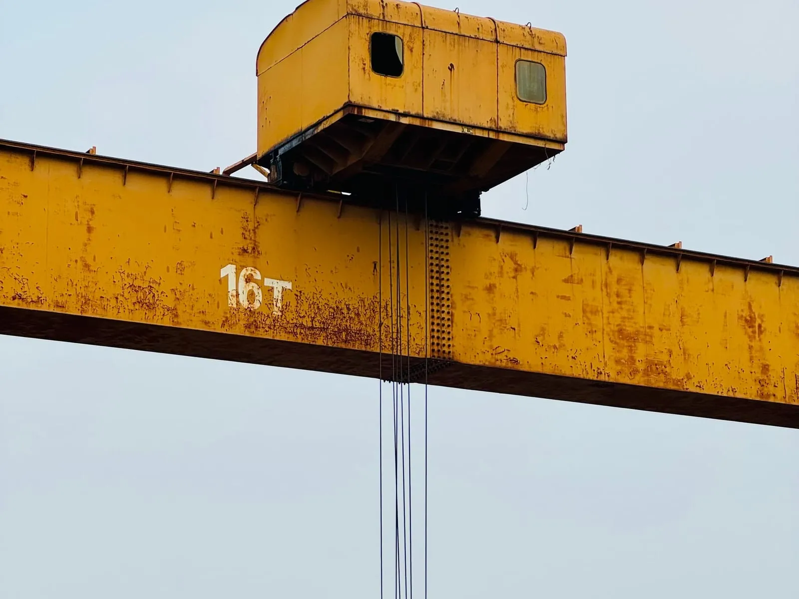Grúa telescópica izando una pieza metálica suspendida por eslingas en una obra industrial